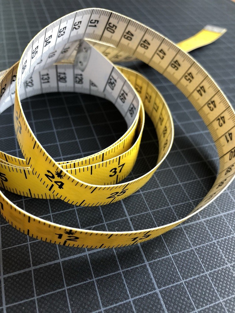 A yellow and white tailors tape measure is laying on a grid table