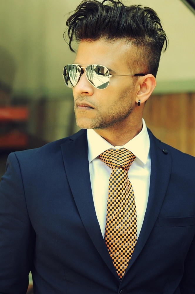 A young businessman in a navy suit and white shirt is wearing a black and gold patterned tie