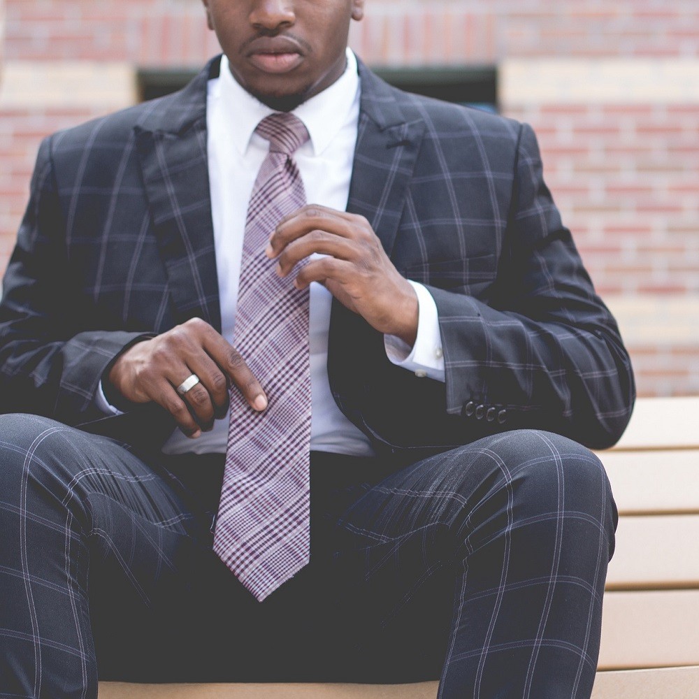 A man in a dark blue suit is wearing a white shirt and pink patterned tie