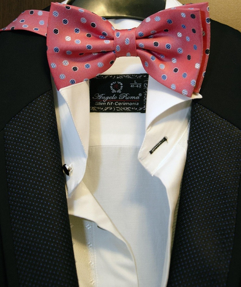 A pink bow tie with blue polka dots is featured on a manakin wearing a black suit and white dress shirt