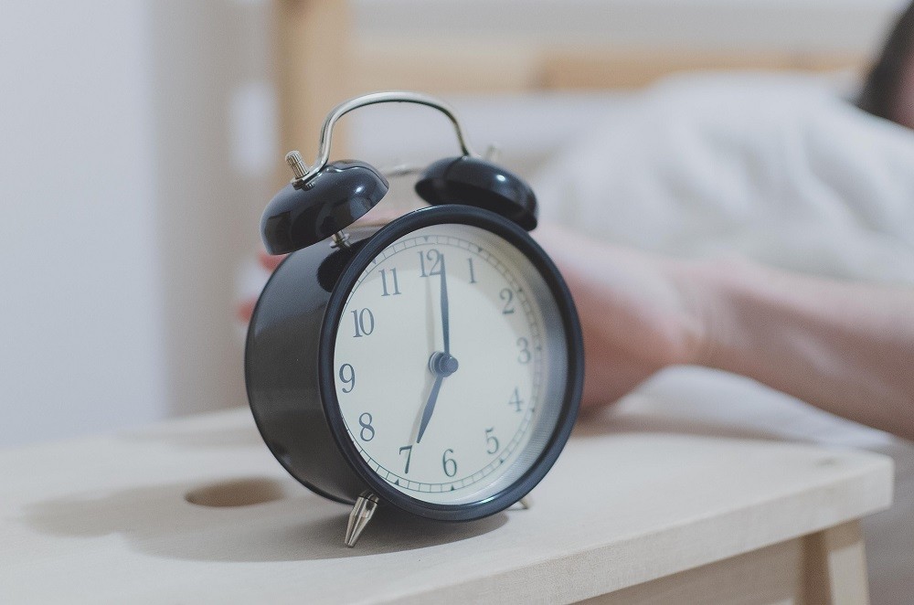 A black analog alarm clock sits on a nightstand