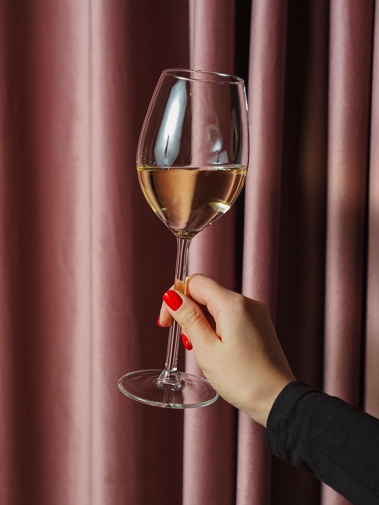 A woman holds a wine glass by the stem (the proper way to hold a wine glass)