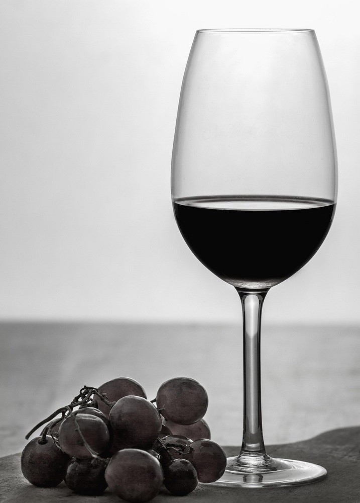 A black and white photograph of a glass of wine and some grapes