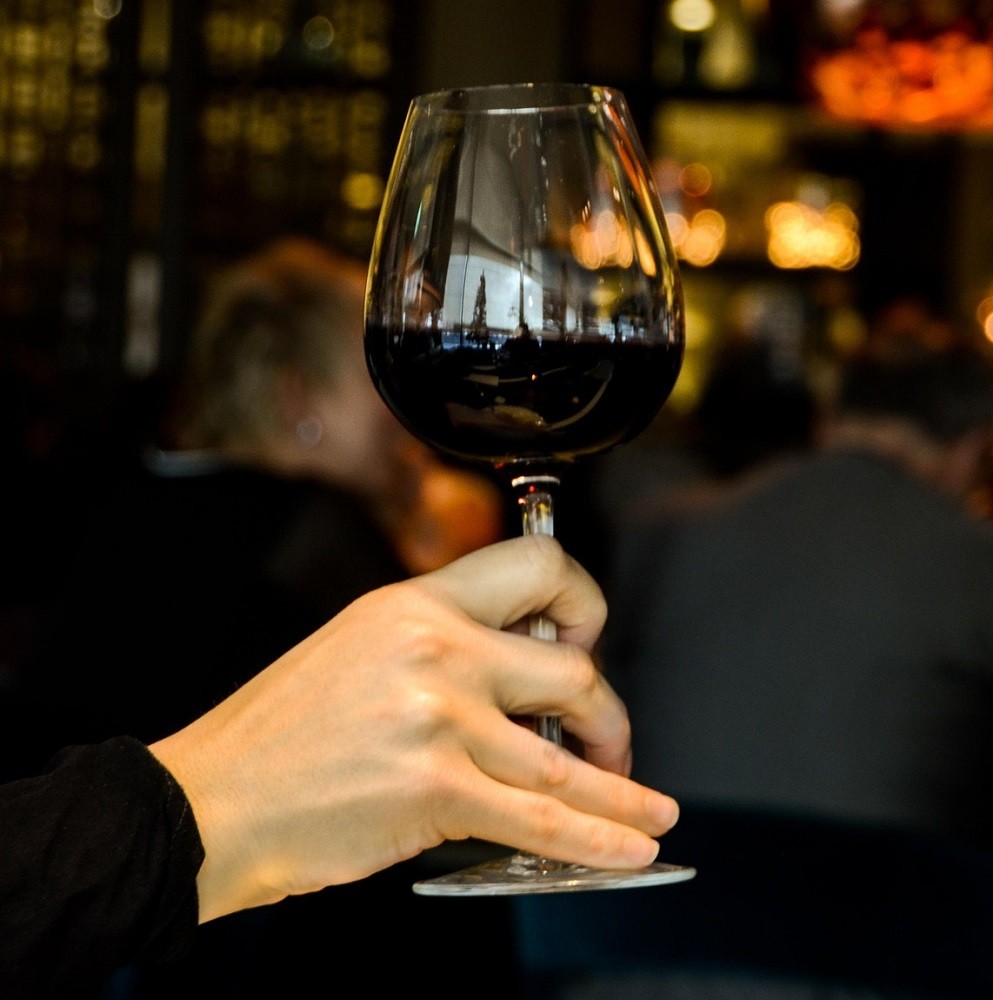 Someone is holding a glass of red wine by the stem, the correct way to hold a wine glass