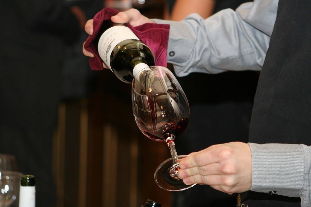 A wine sommelier is pouring wine from a bottle in to a wine glass