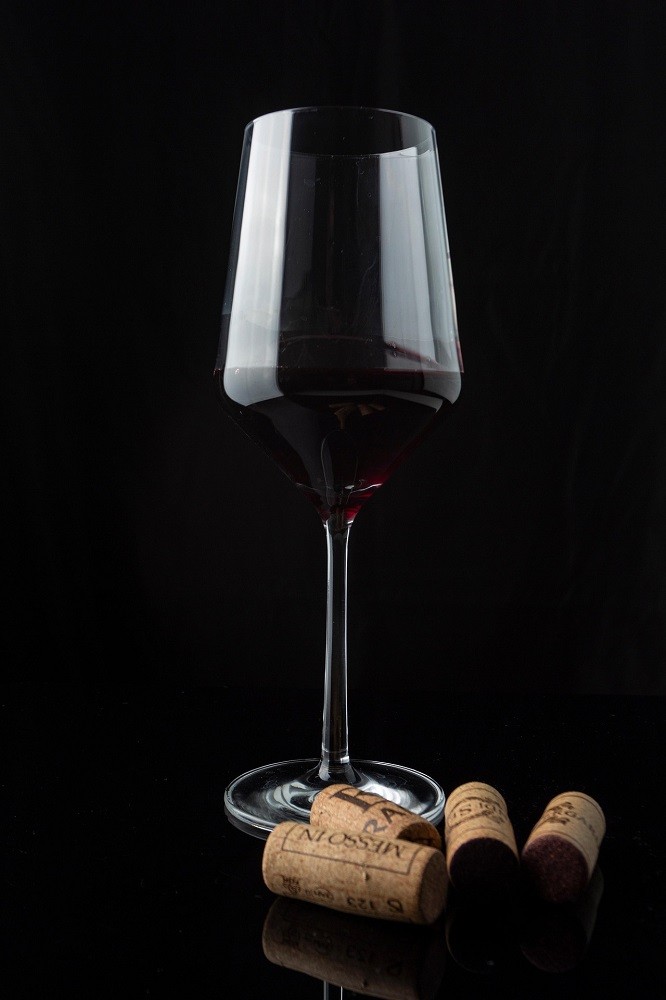 A red wine glass with four wine corks beside it