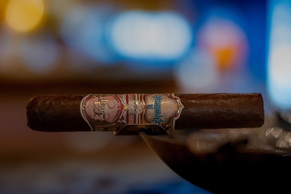 An unlit brown cigar sits on the side of an ashtray