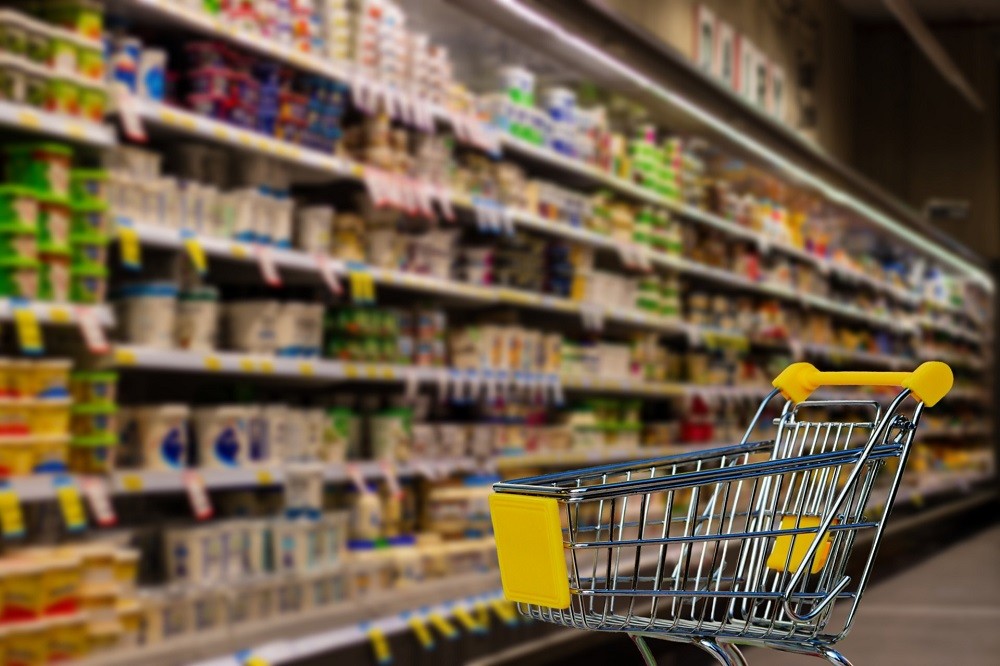 A silver shopping cart sits in front of shelves stocked with food
