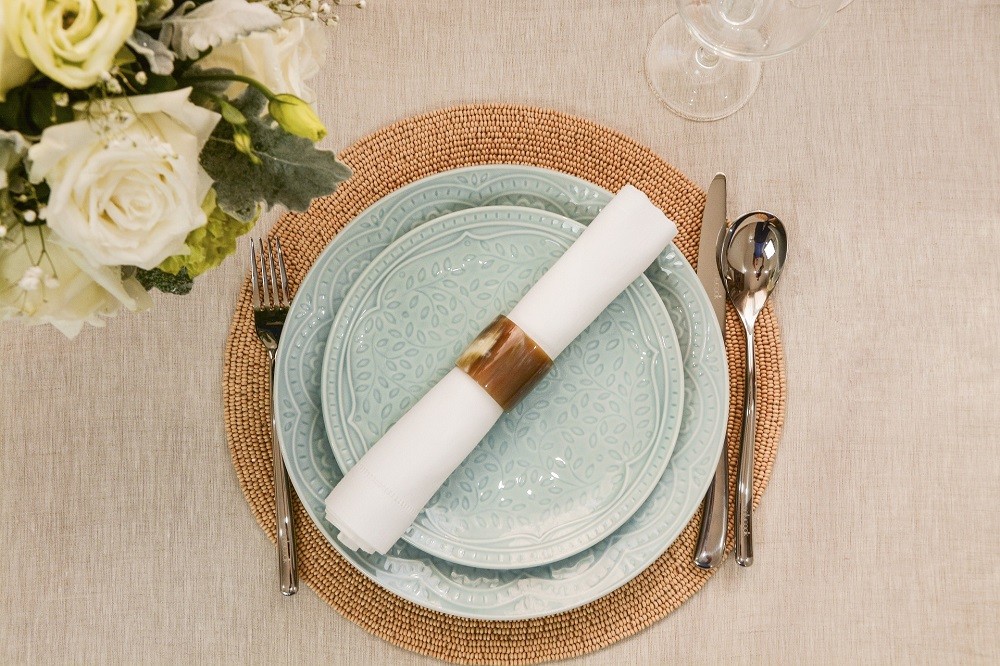 A white napkin with a brown napkin ring sits on a light-blue plate at a dinner table