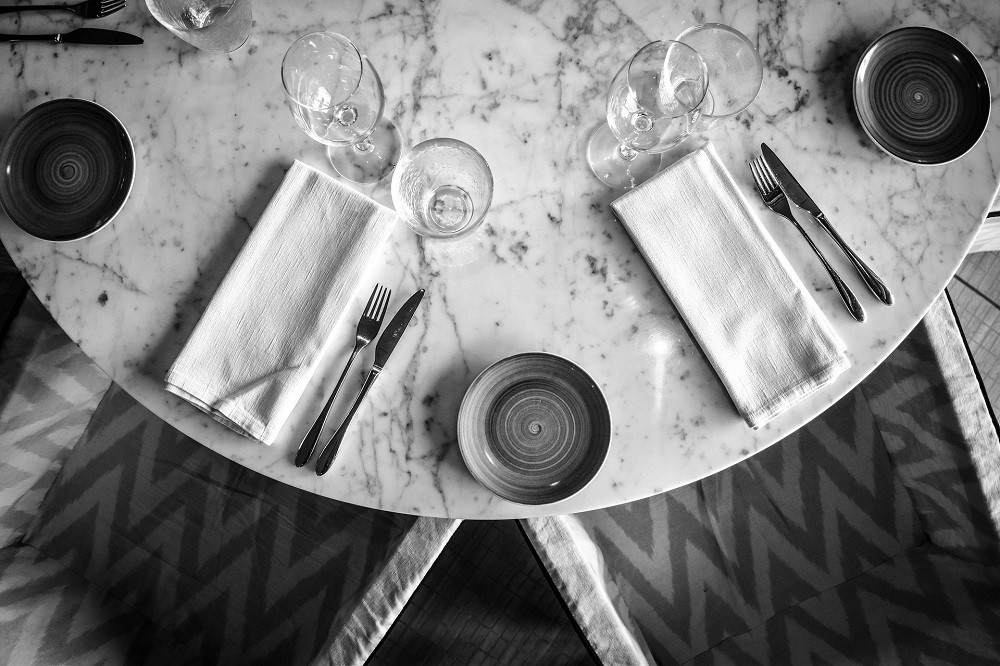 A black and white photograph of a semi-formal place-setting with a napkin, silverware, and glasses