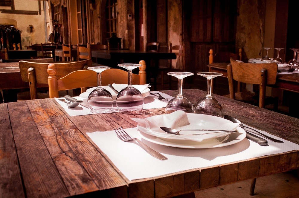A place-setting at a restaurant shows 2 seats with plates, silverware, glasses, and napkins