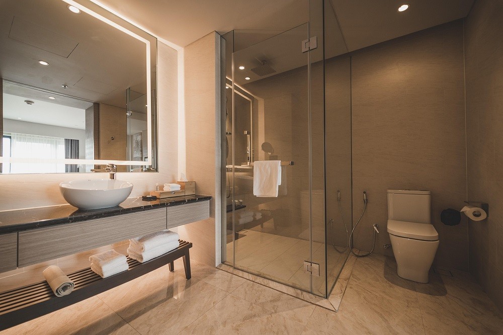 A luxury bathroom featuring a glass shower, large mirror, and several decorative towels