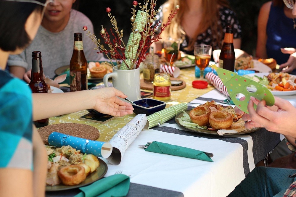 A group of people sit at a dining table. The table has numerous plates, glasses, and party favours on it