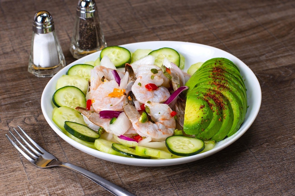 A salad with shrimp, avocado, and cucumbers is accompanied by both the salt and pepper shakers