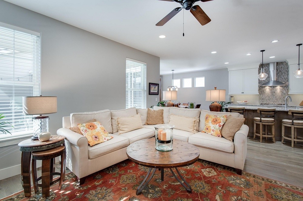 An open house showing the living room with a white couch, brown tables, white walls, and a red rug