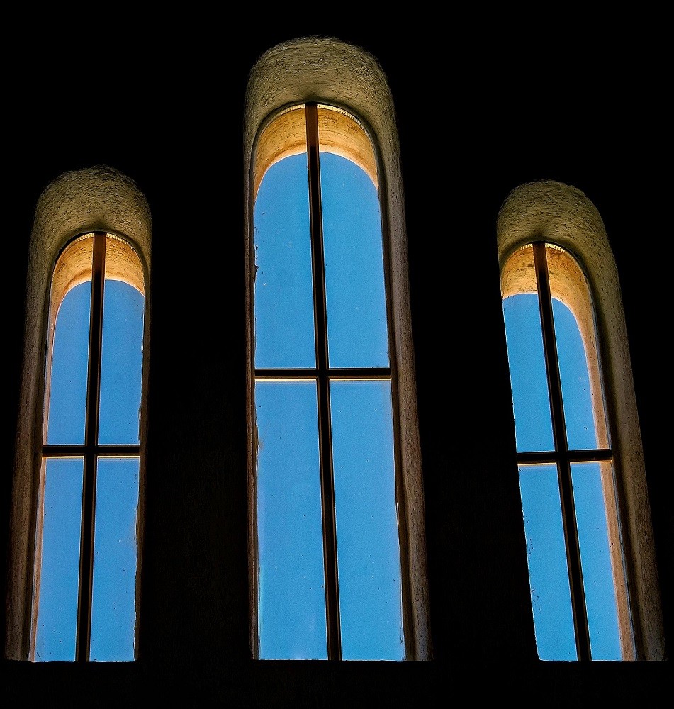 Interior view from a church through three large windows with a blue sky outside