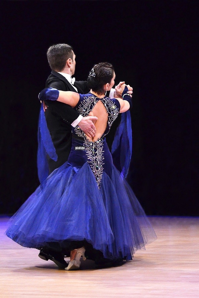 A woman wearing a blue dress is dancing with a man in a tuxedo. Dancing is a skill that requires character