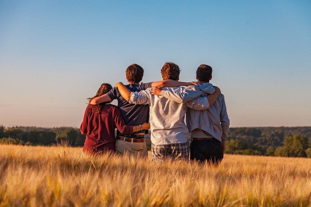 A group of friends are facing away from the camera. Each one has their arms around the person on each side of them