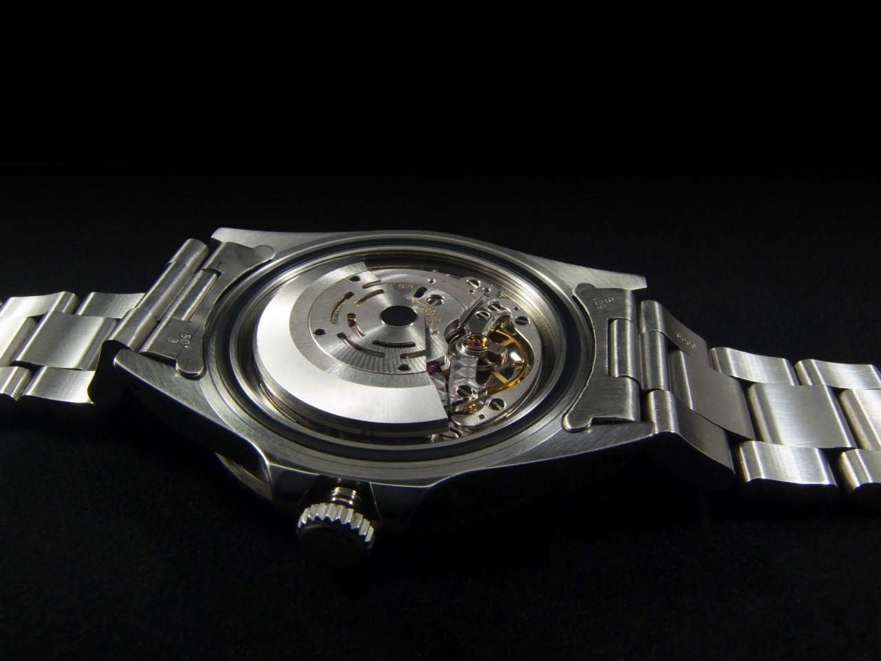 A watch has its back cover removed, revealing an automatic movement. The rotor (the part that spins to 