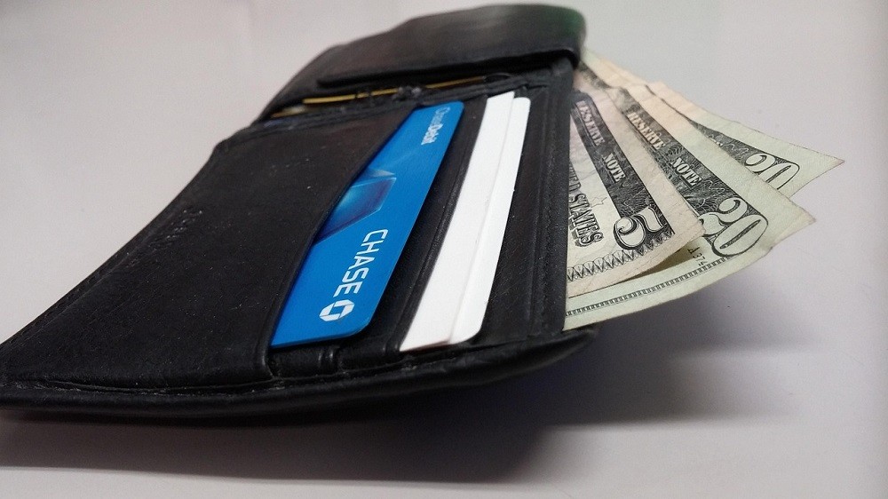 Splitting the bill on a first date is common. A wallet is open sitting on a table. There are some credit cards and dollar bills inside
