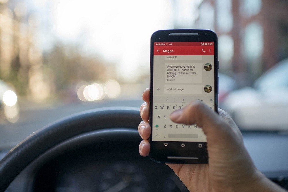 A phone is held up near a steering wheel. The driver is checking their phone and not paying attention to the road. This is very dangerous