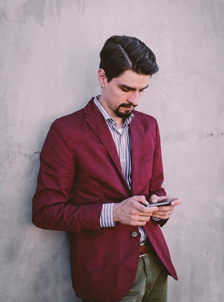 A young businessman wearing a burgundy suit is texting on his smartphone