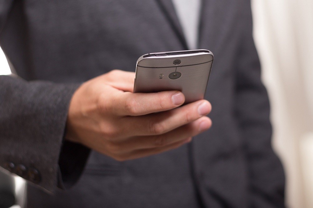 A man in a grey suit is holding a smartphone