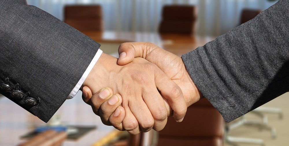 Two businessmen in suits are shaking hands with a firm, but not too firm, grip. This is a proper handshake