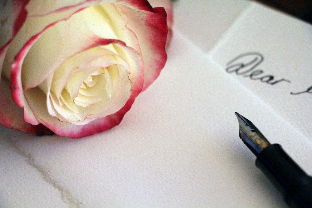 A rose and fountain pen sit on thick card stock about to write a love letter